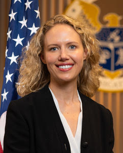 Whitney Lohmeyer stands in front of an American flag and FCC crest, smiling, in an official headshot