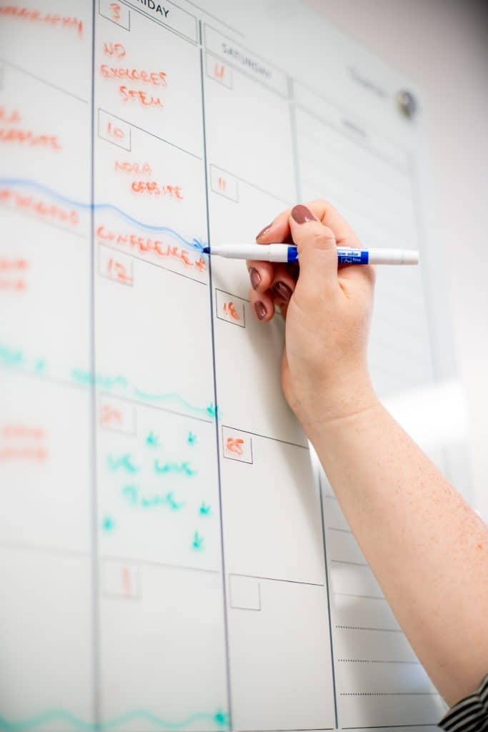 Photo includes an arm raised to a white board, adding a mark to the calendar. Photo by Angie Hubert, Notre Dame Research