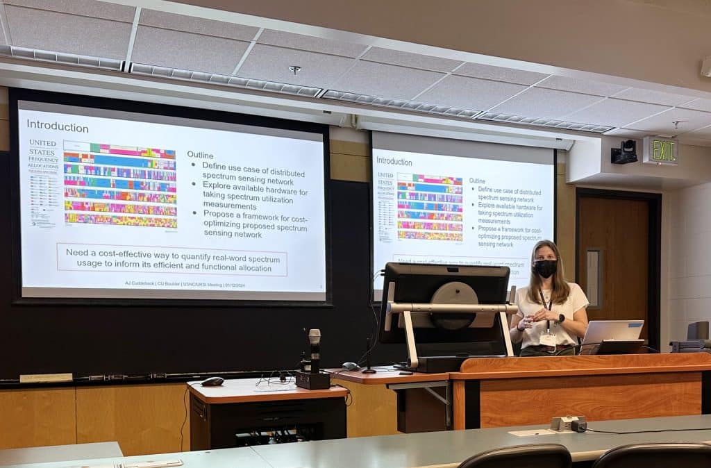 Laila Fighera Marzall stands at the front of a room, wearing a mask, with her presentation at NRSM 2024.