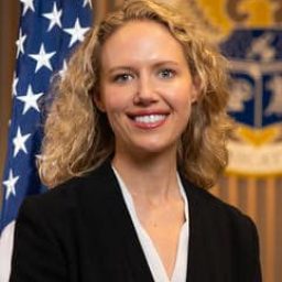 Whitney Lohmeyer stands in front of an American flag and FCC crest, smiling, in an official headshot